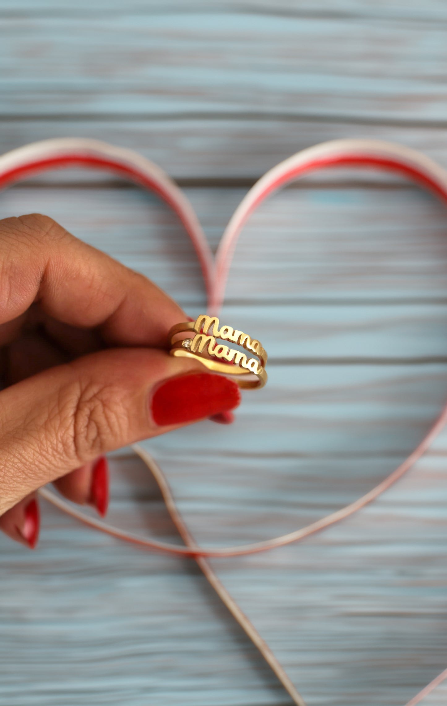 Hand holding gold Mama rings over a heart-shaped cutout on a light blue background