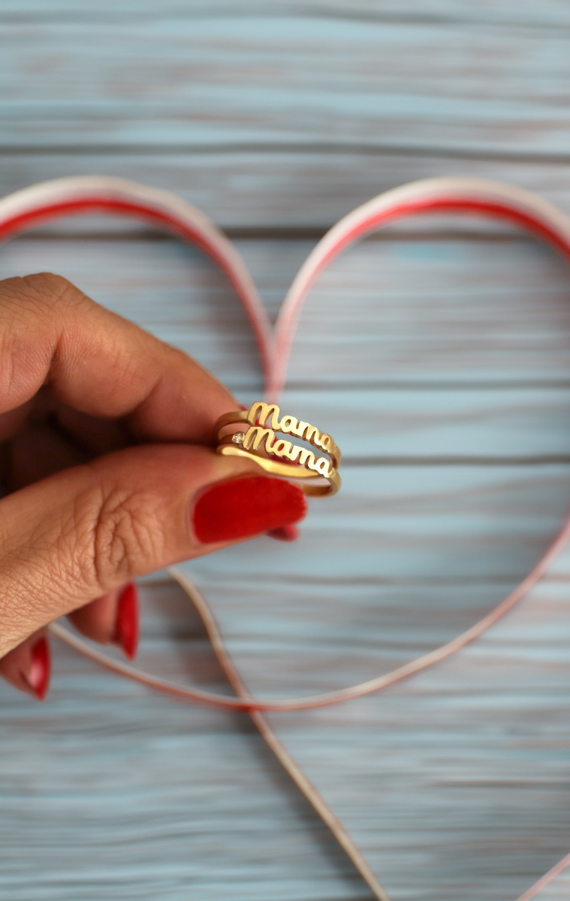 Hand holding gold Mama rings over a heart-shaped cutout on a light blue background