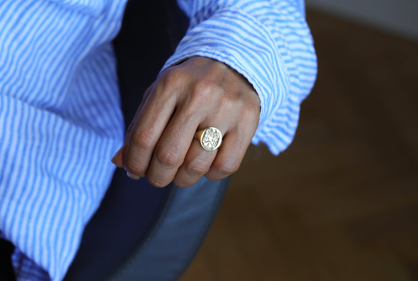 engraved gold signet ring on a man's  handwith a blue striped shirt in the background