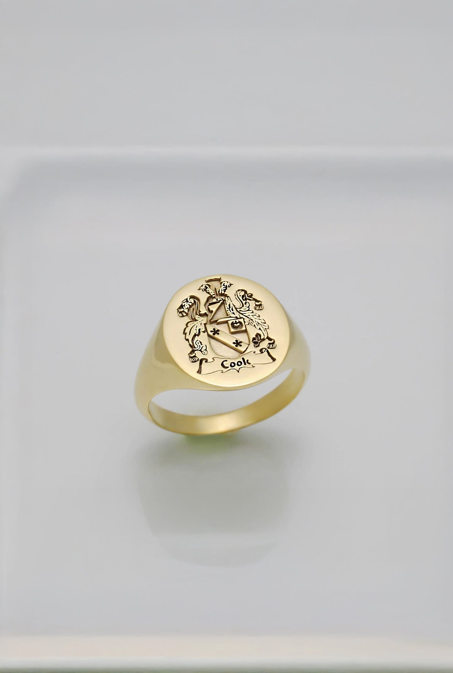 solid gold ring with engraved coat of arms design on a light gray background