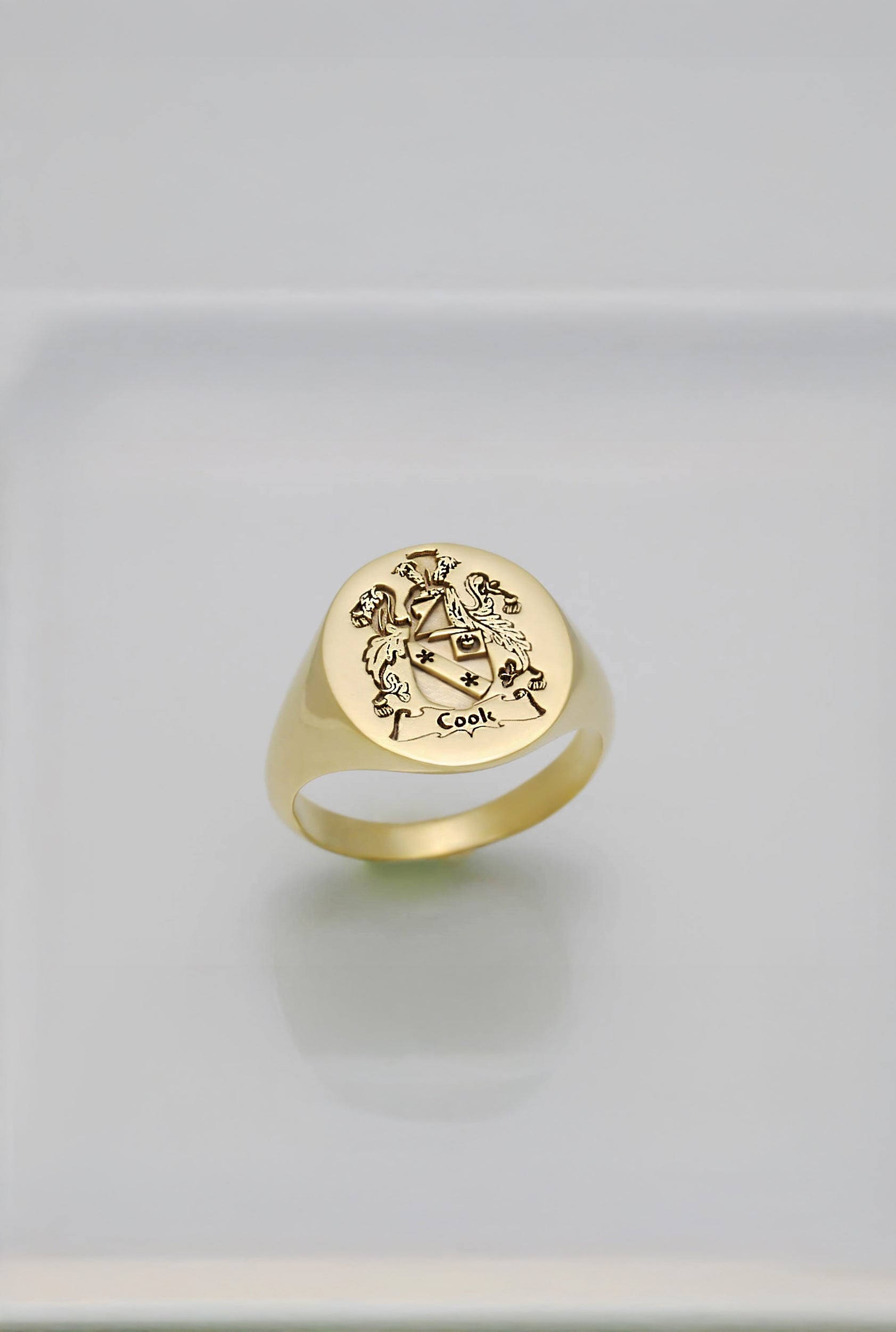 solid gold ring with engraved coat of arms design on a light gray background