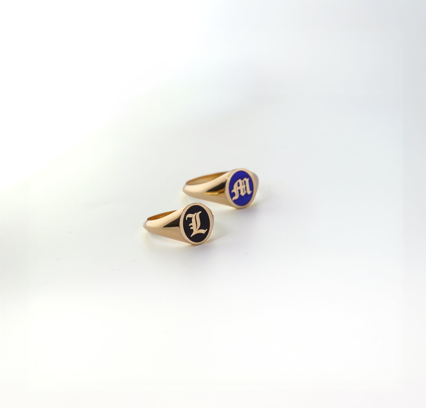 Two gold initial rings with blue and black enamel on a white background