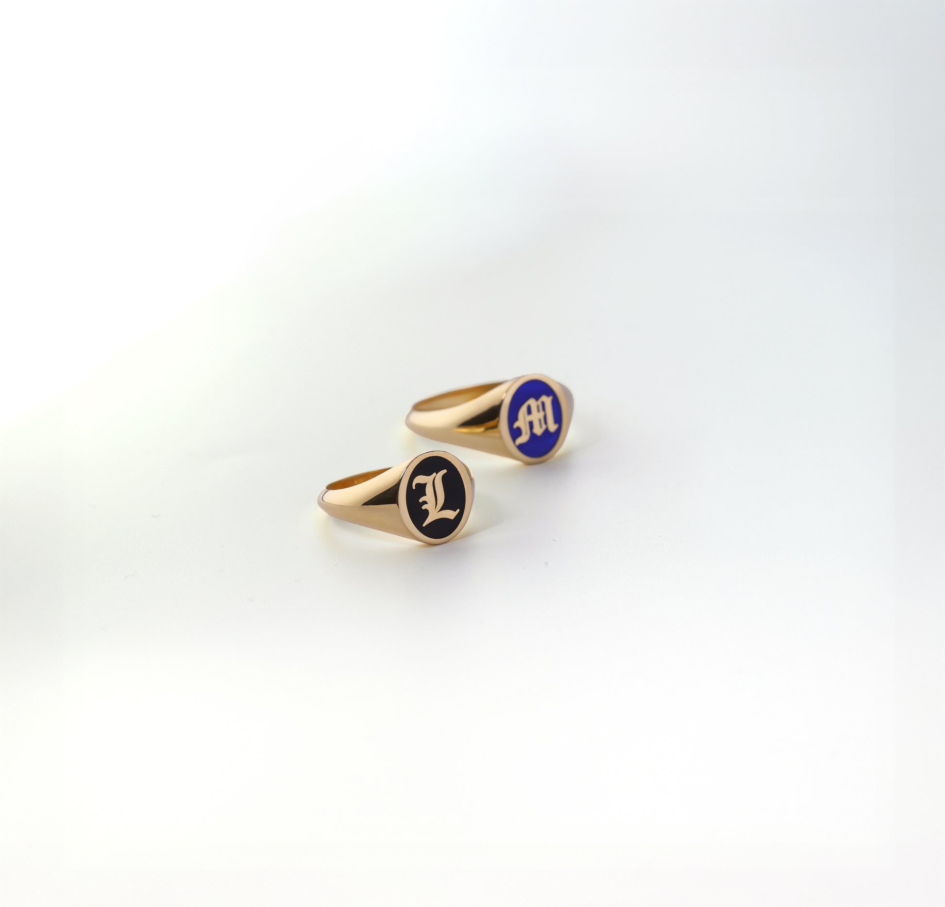 Two gold initial rings with blue and black enamel on a white background