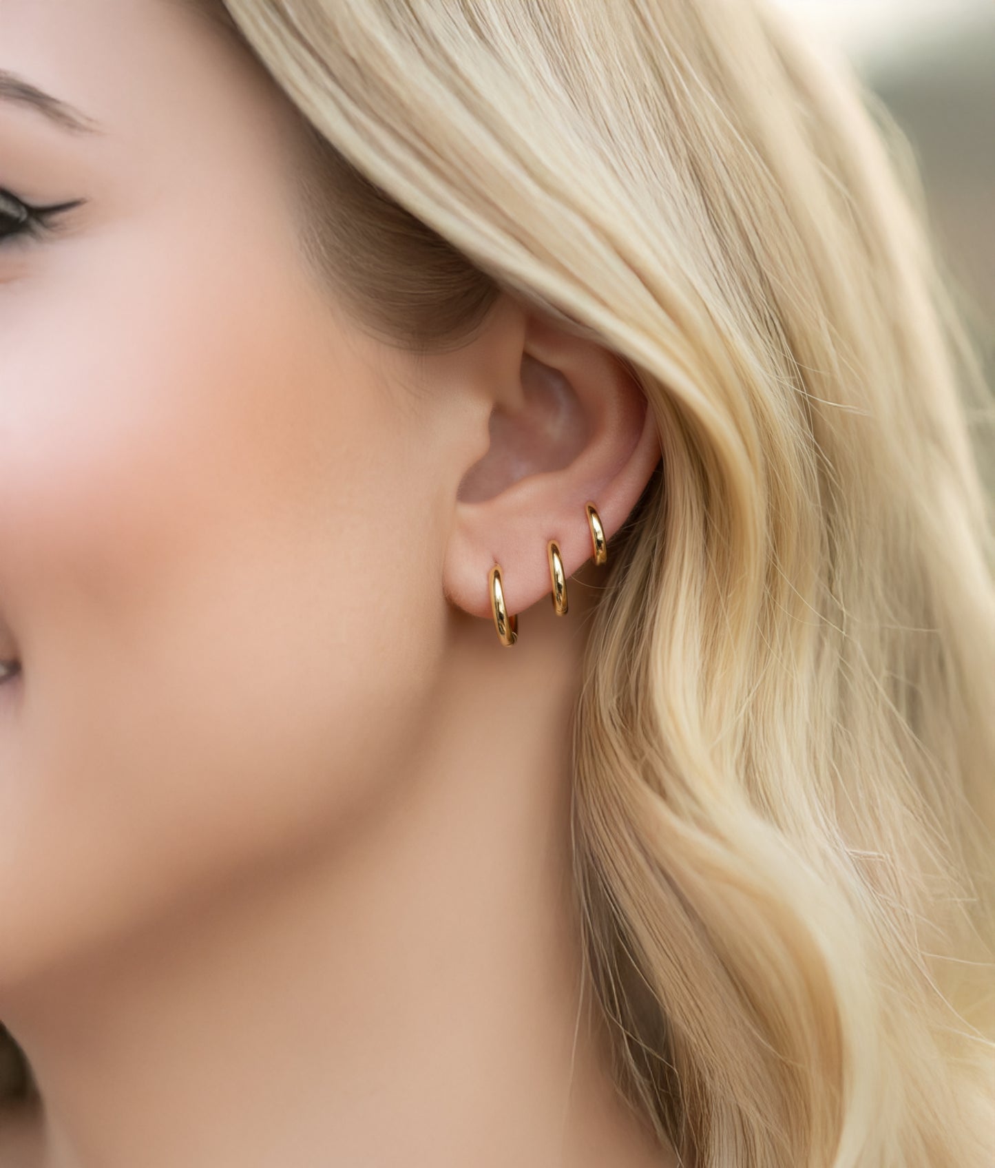 Close-up of a model wearing gold hoop earrings with blurred background