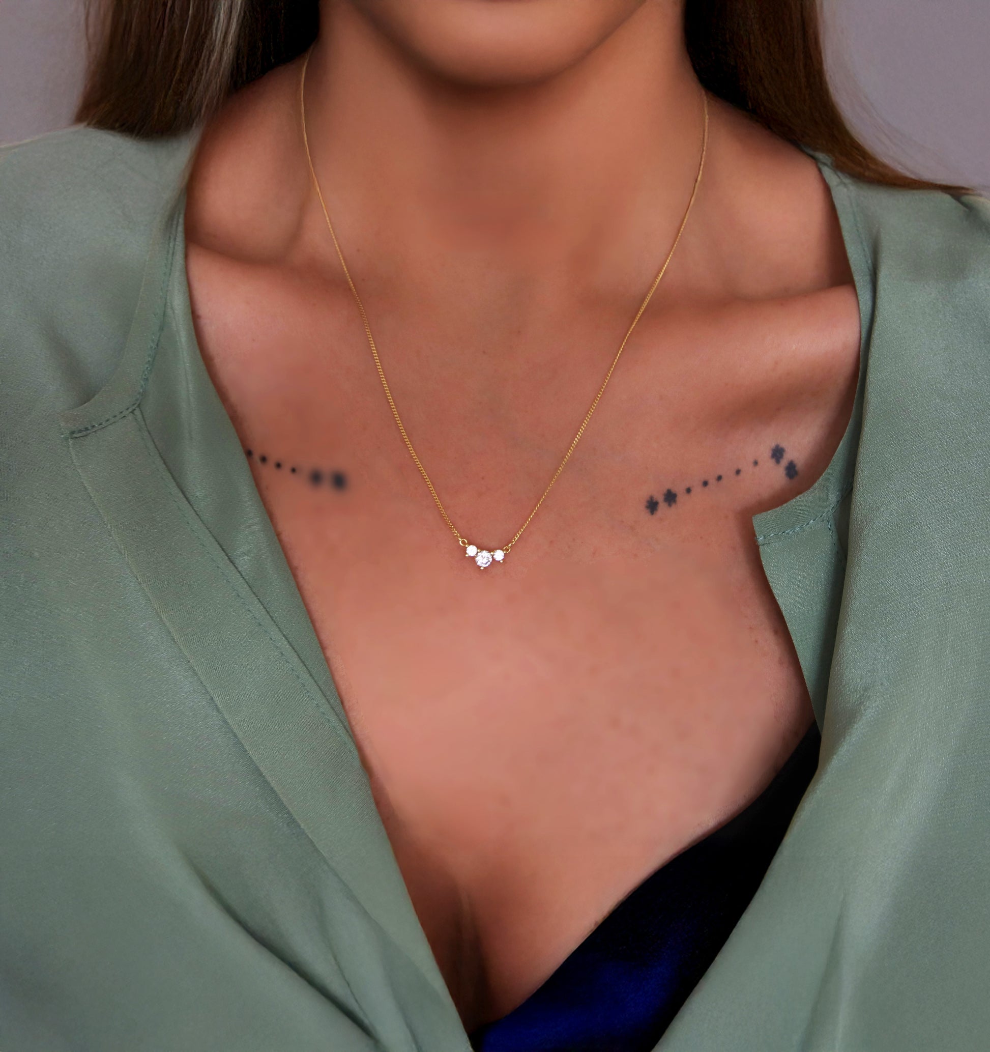 Close-up of a woman wearing a gold necklace with a small pendant with 3 cz stones.