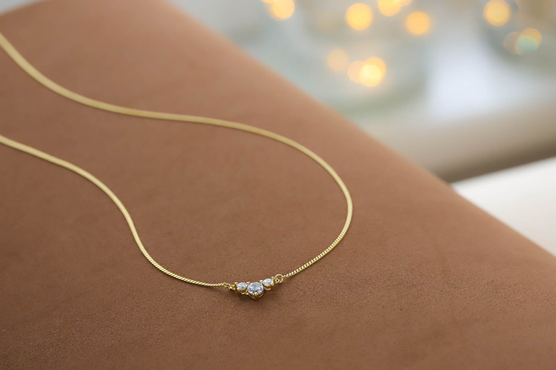 Close up of the delicate gold chain and 3 stone cz pendant resting on a textured brown surface.