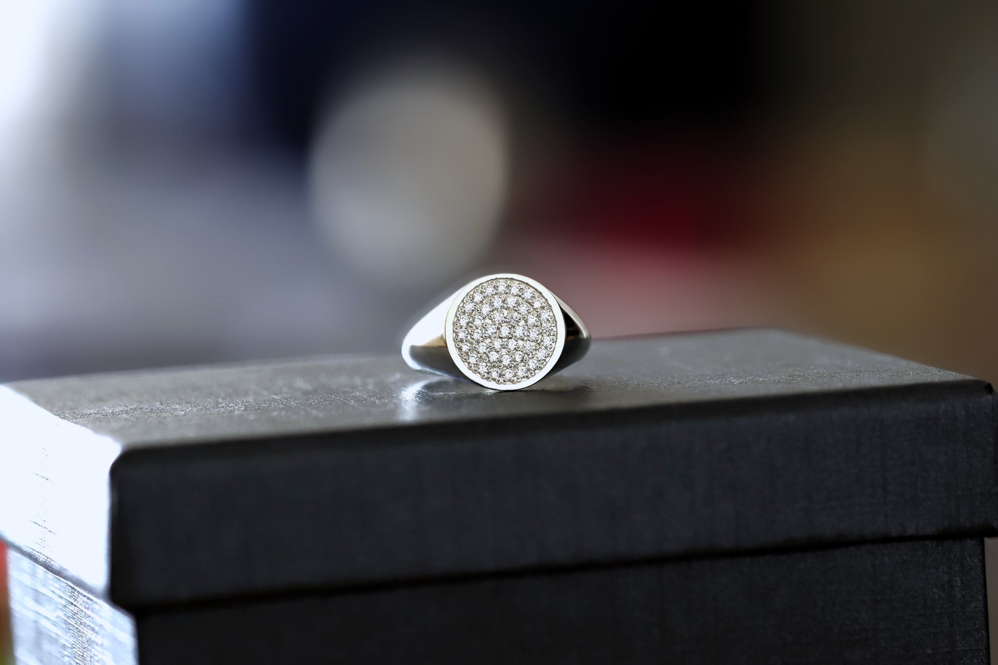 Silver signet ring with diamonds on a black box against a blurred background