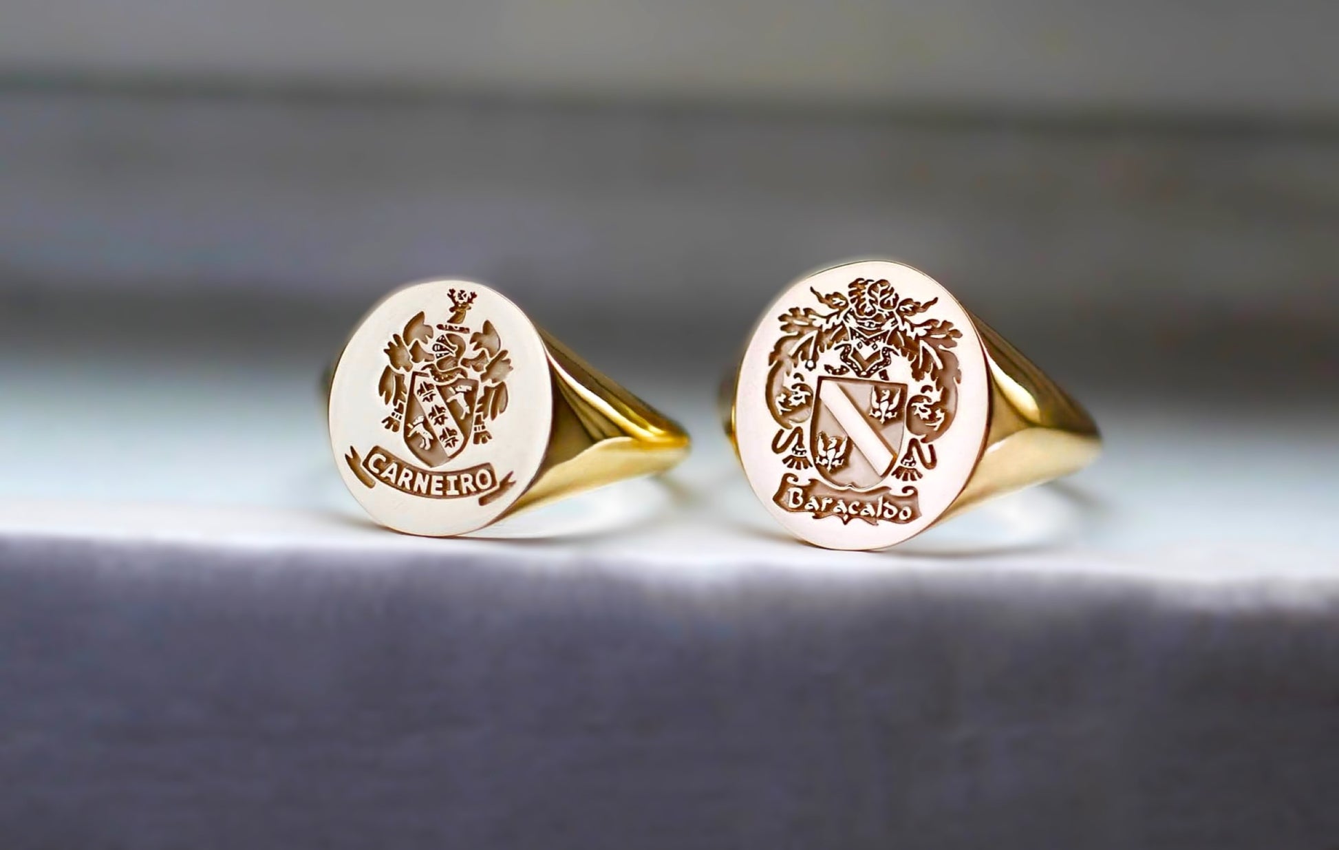 close-up of two gold signet rings with engraved family coat of arms designs on a gray background
