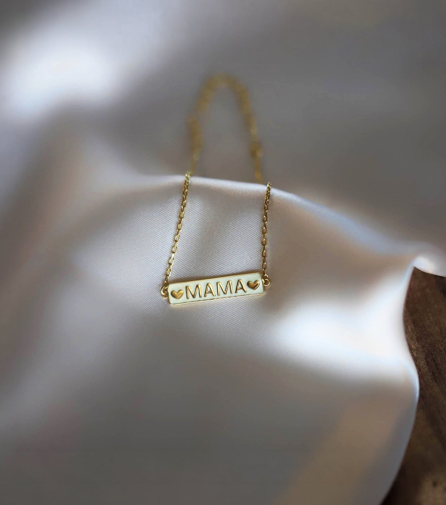 The solid gold mama bracelet resting beautifully on smooth white silk fabric.