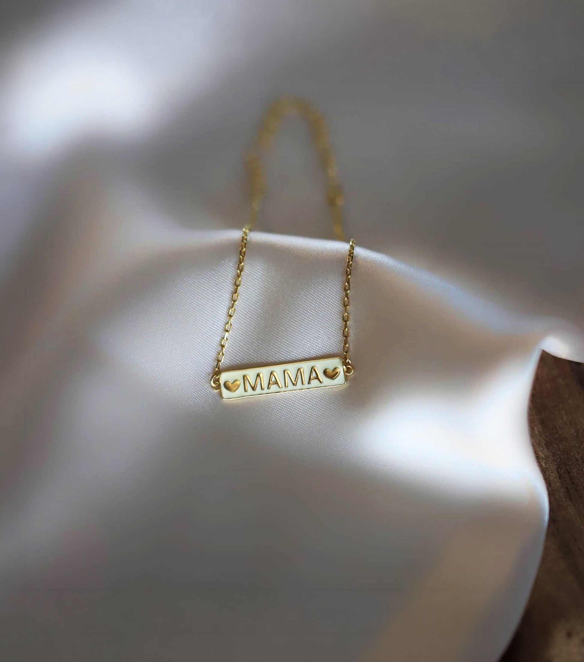 The solid gold mama bracelet resting beautifully on smooth white silk fabric.