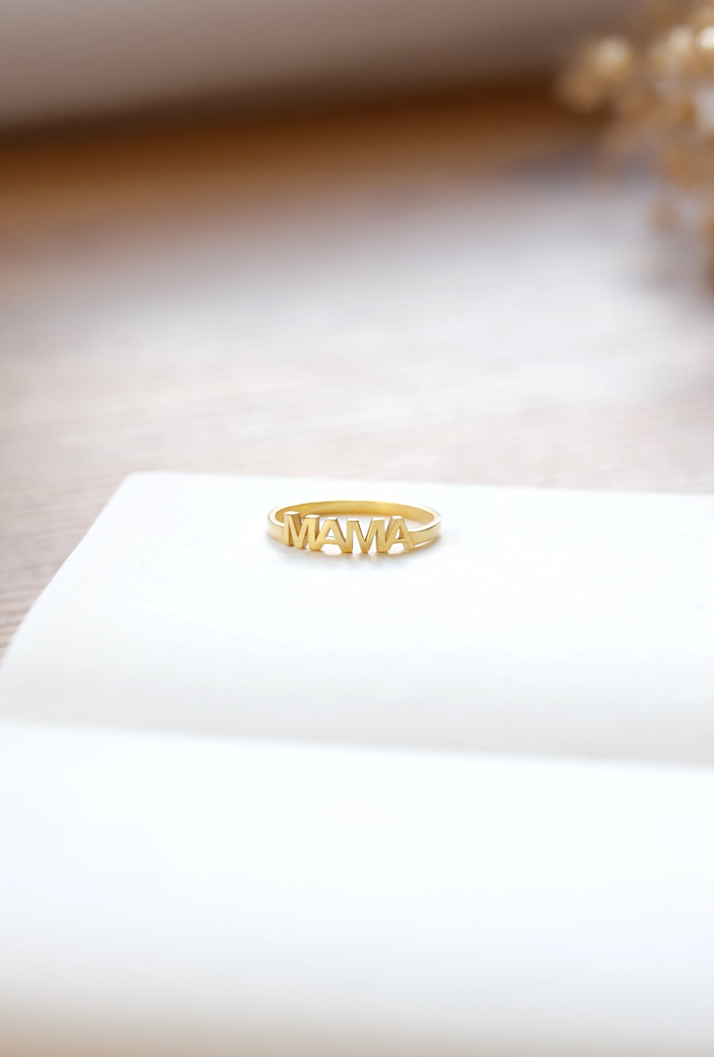 Gold ring with 'MAMA' on a white surface