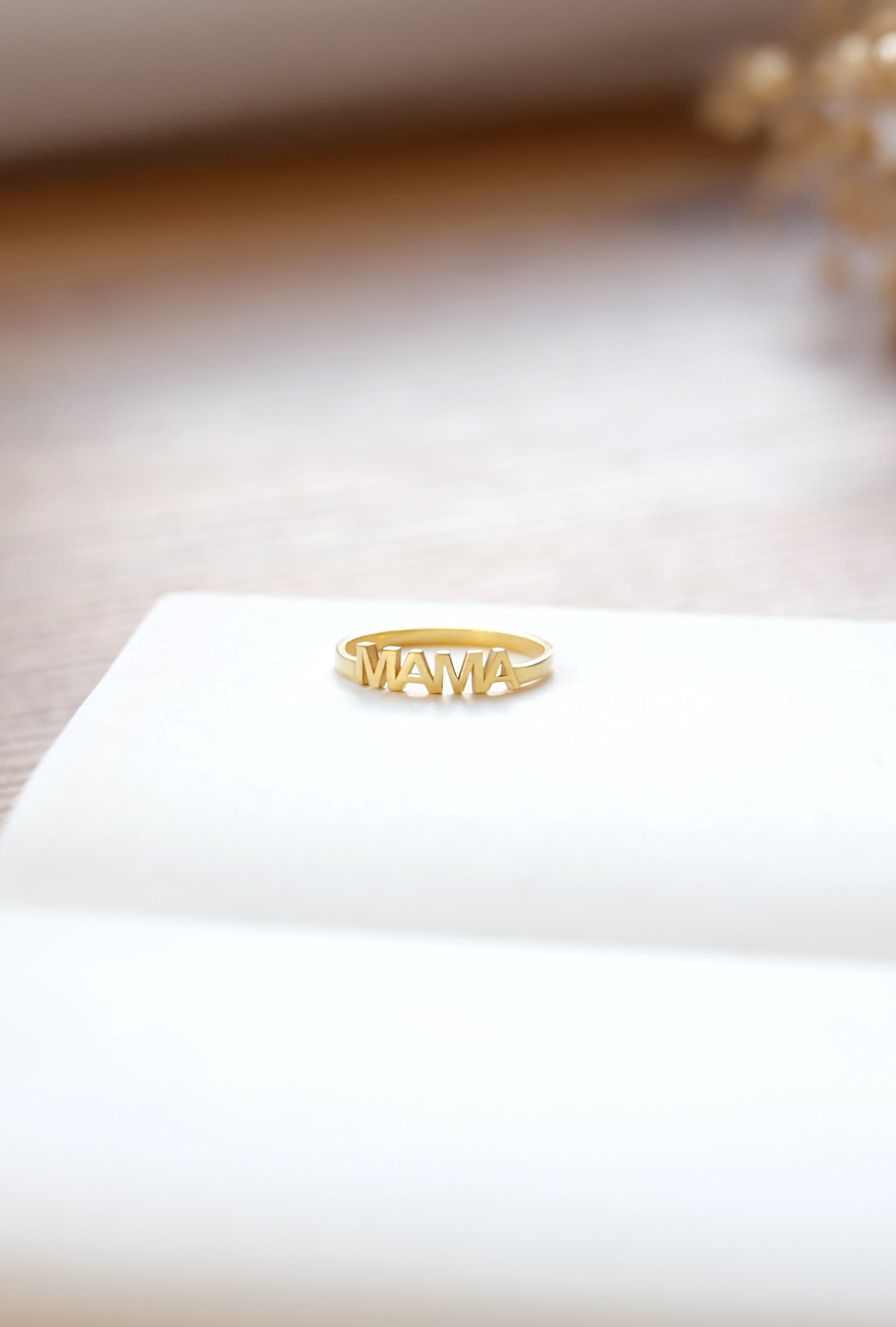 Gold ring with 'MAMA' on a white surface