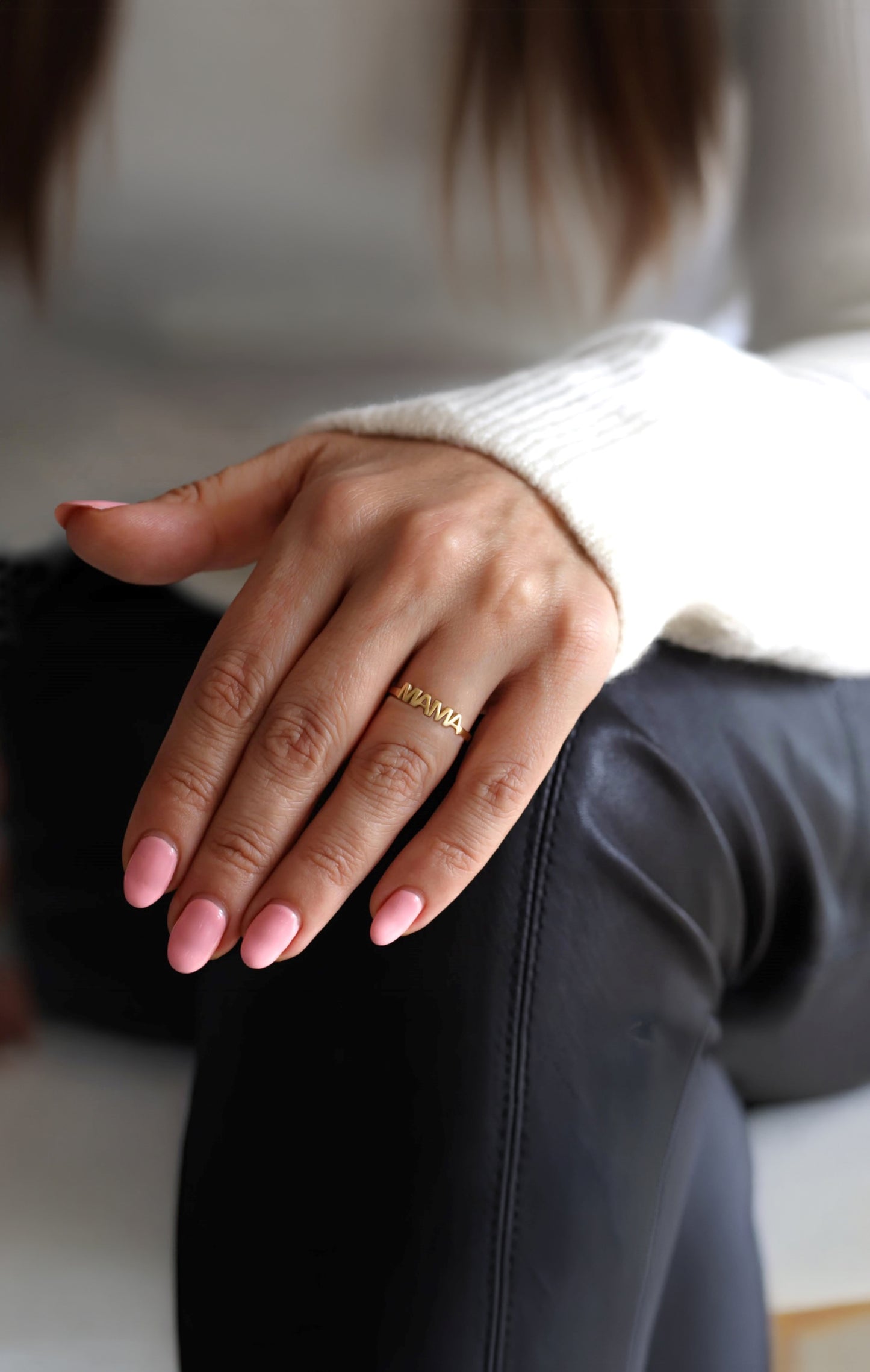 Close-up of a woman's hand wearing a gold MAMA ring with a blurred background