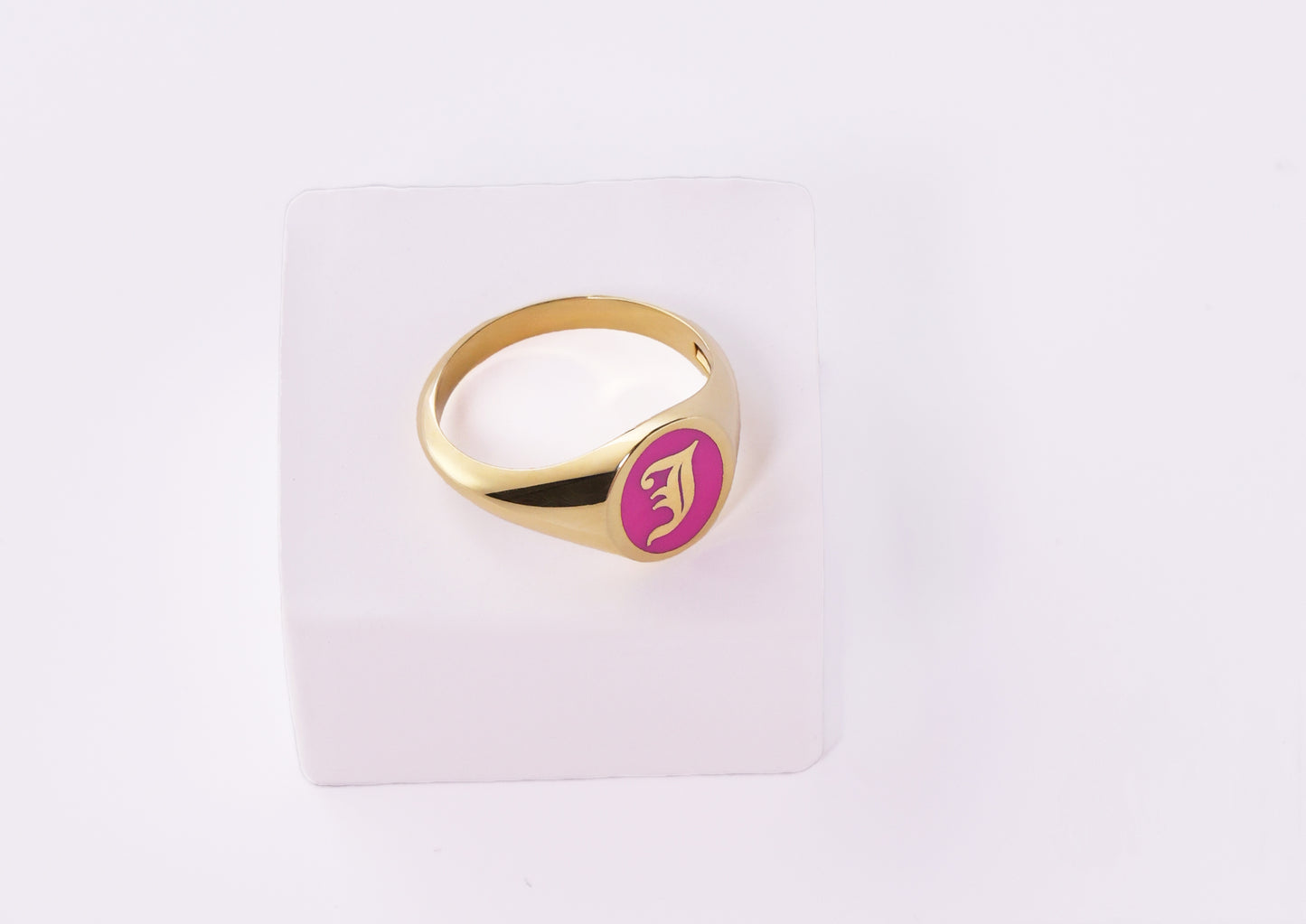 Gold signet ring with pink enamel and J initial on a white background