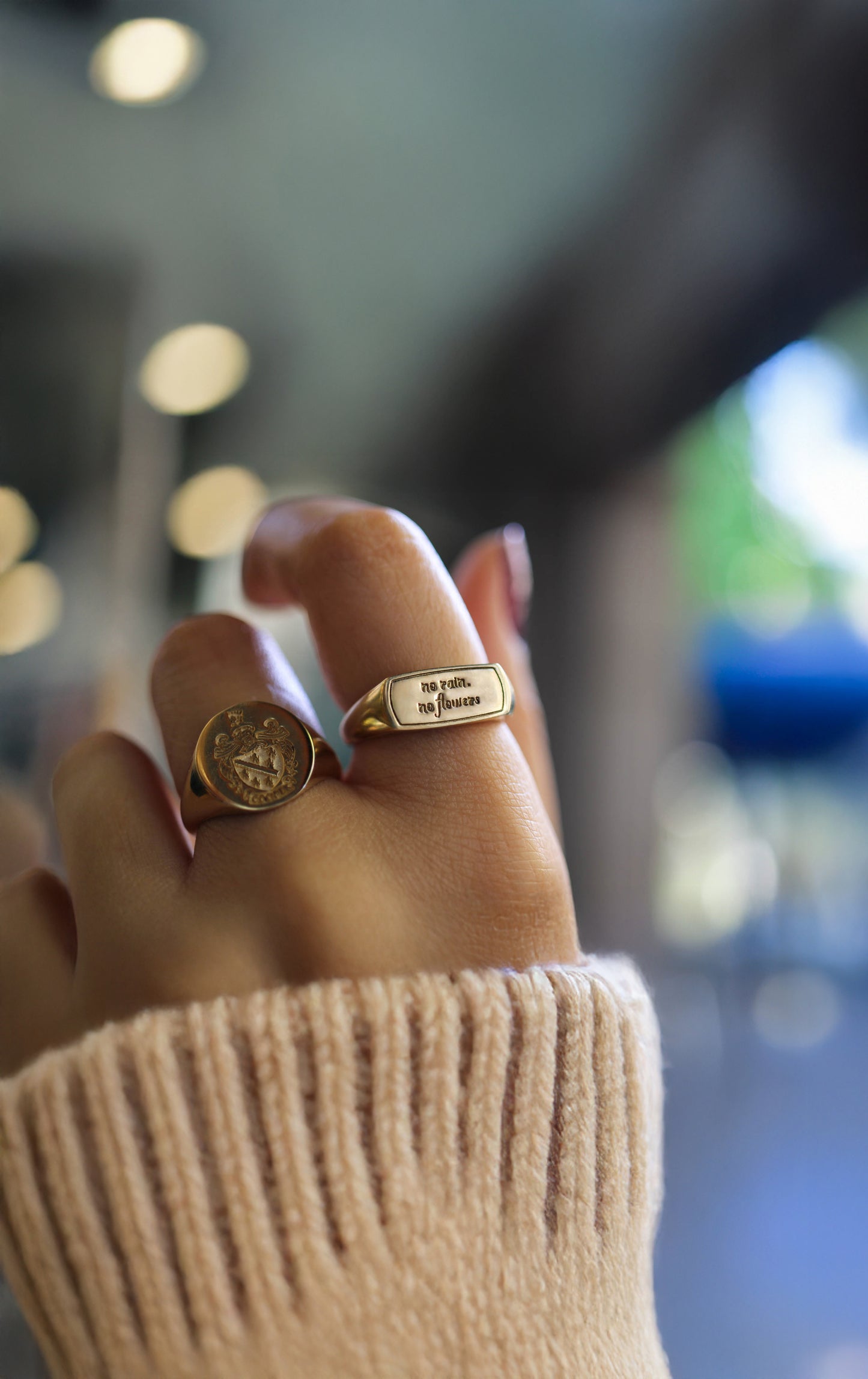 Woman's hand wearing a solid gold custom engraved signet ring featuring the inspirational quote no rain no flowers.