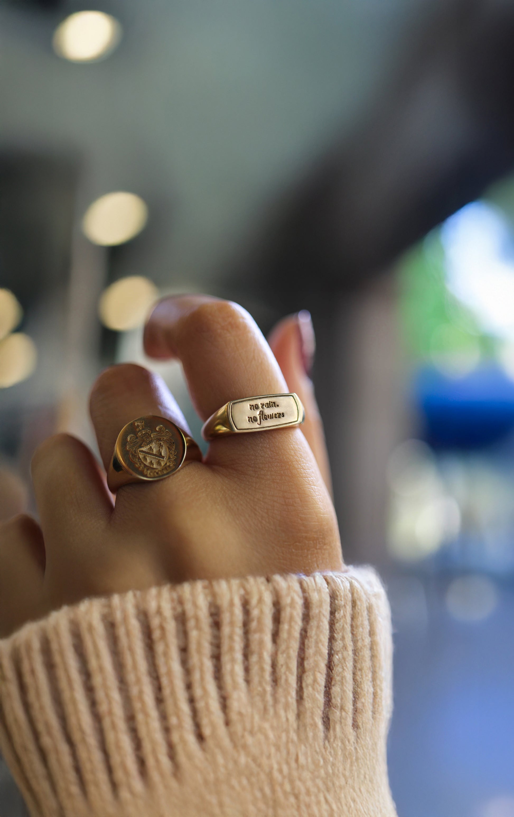 Woman's hand wearing a solid gold custom engraved signet ring featuring the inspirational quote no rain no flowers.