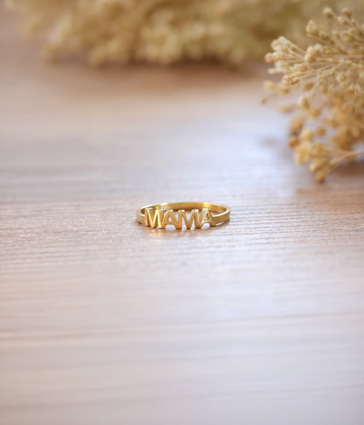Gold ring with 'MAMA' on a textured surface 