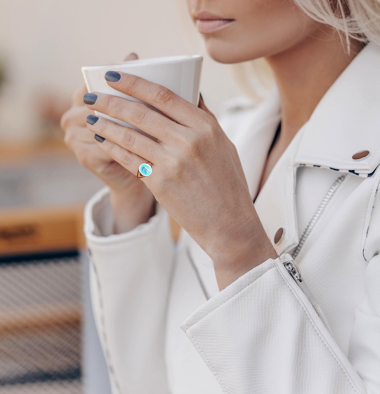 woman's hand wearing a personalized pinky ring, holding a white mug with a blurred background