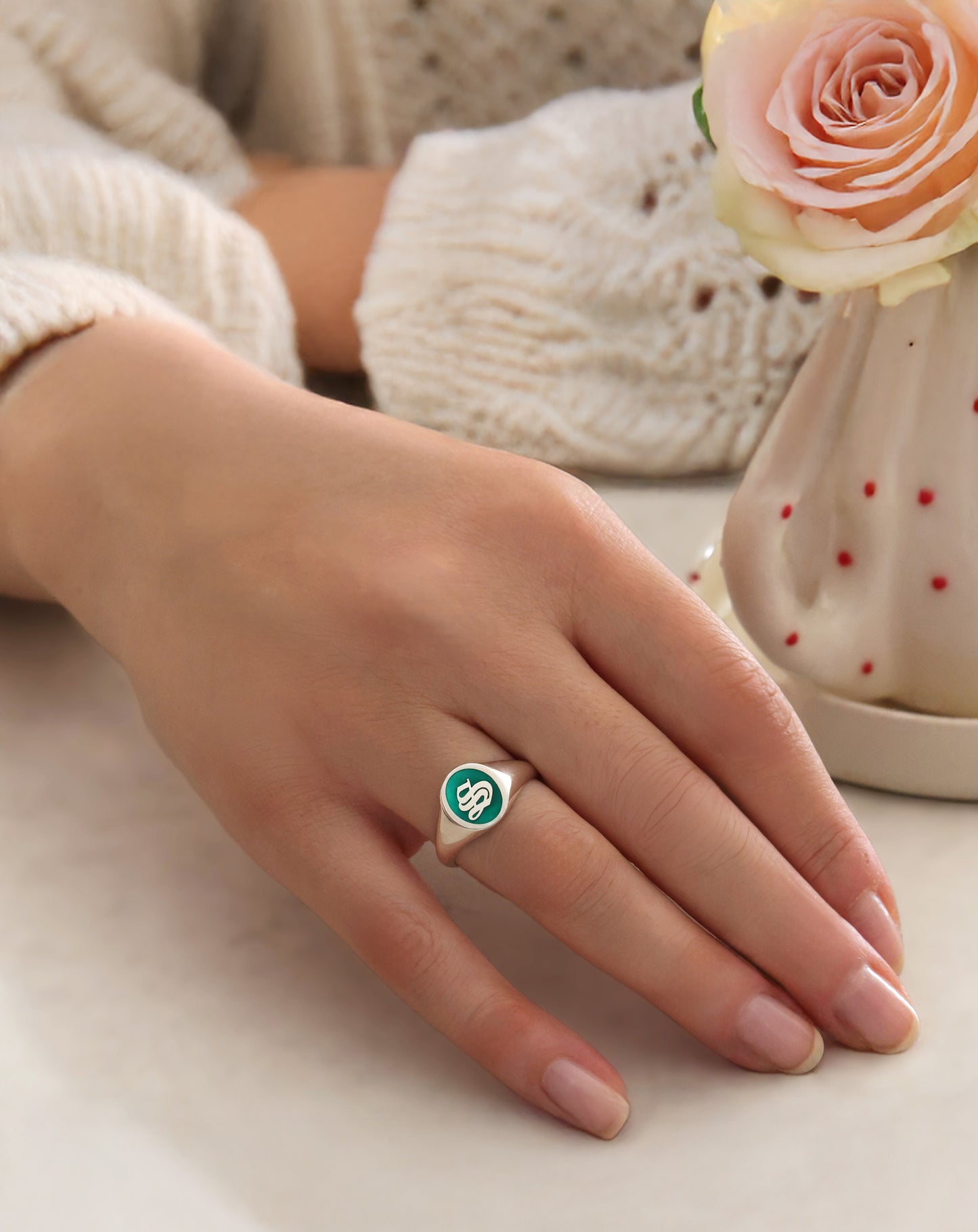 initial signet ring with green enamel worn on woman's hand.
