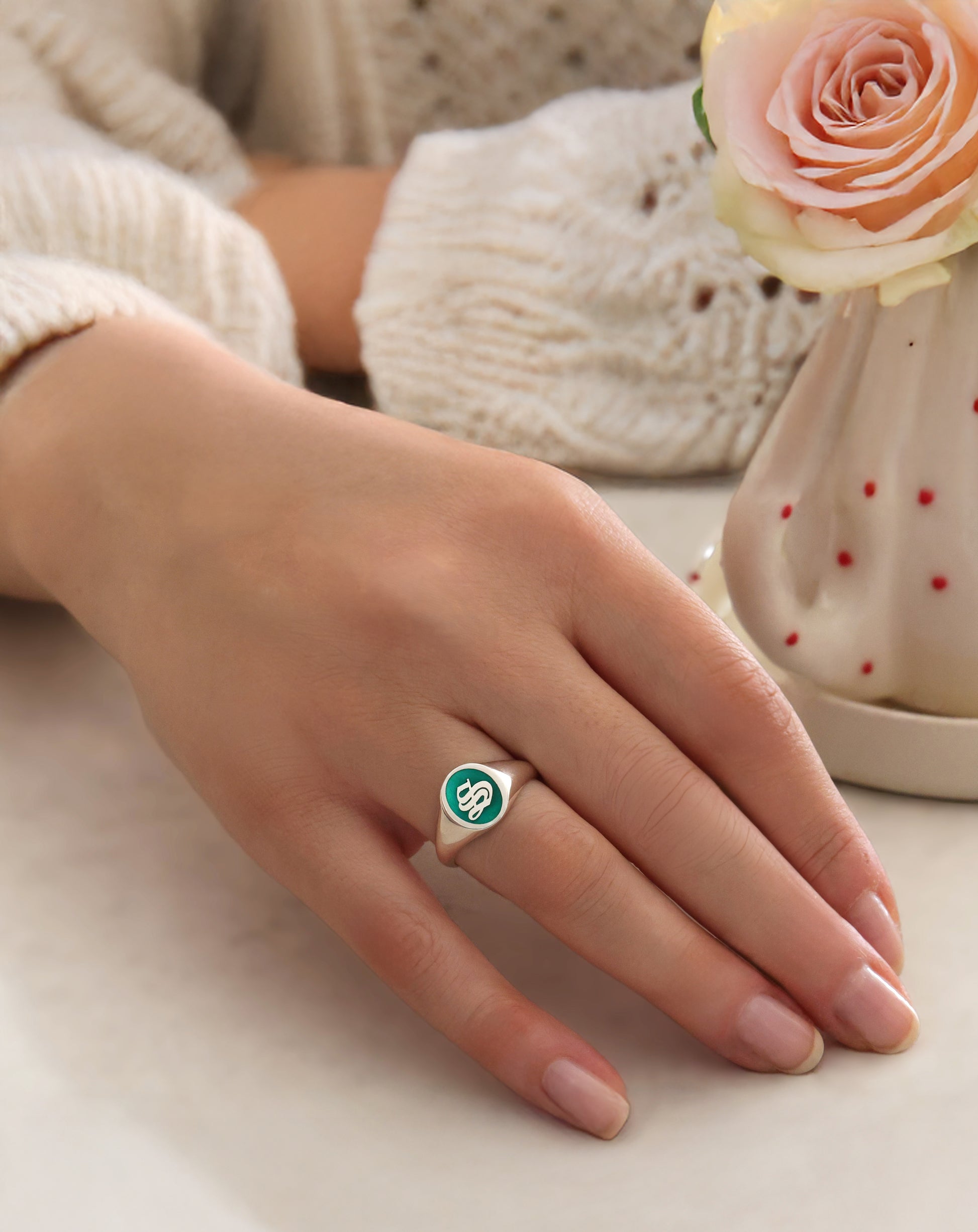 initial signet ring with green enamel worn on woman's hand.
