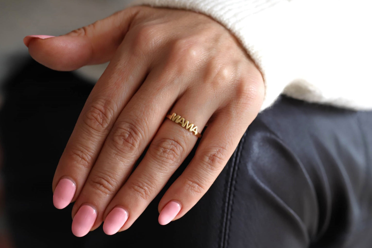 A gold ring with MAMA on it on a female model's hand.