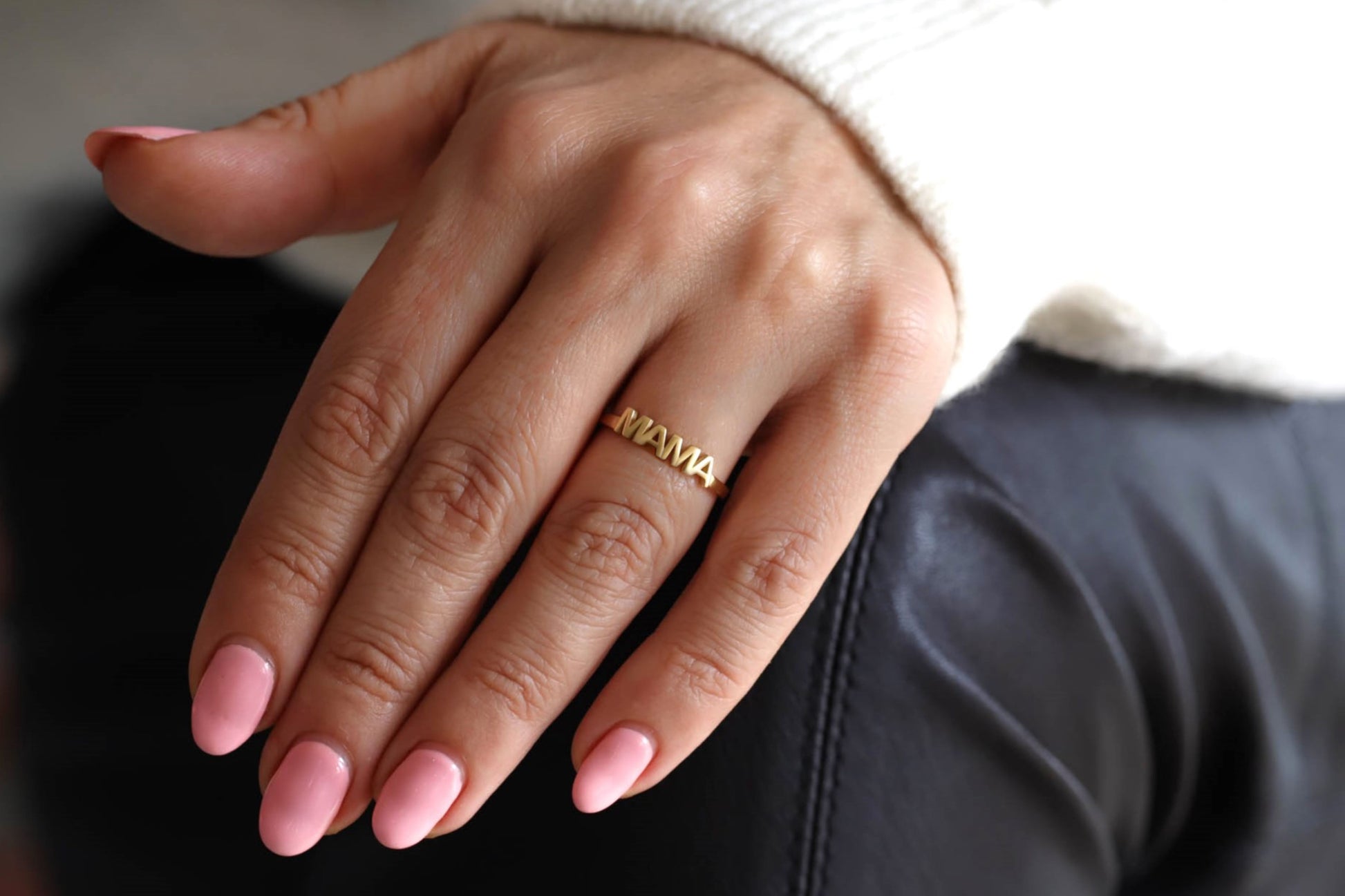 A gold ring with MAMA on it on a female model's hand.