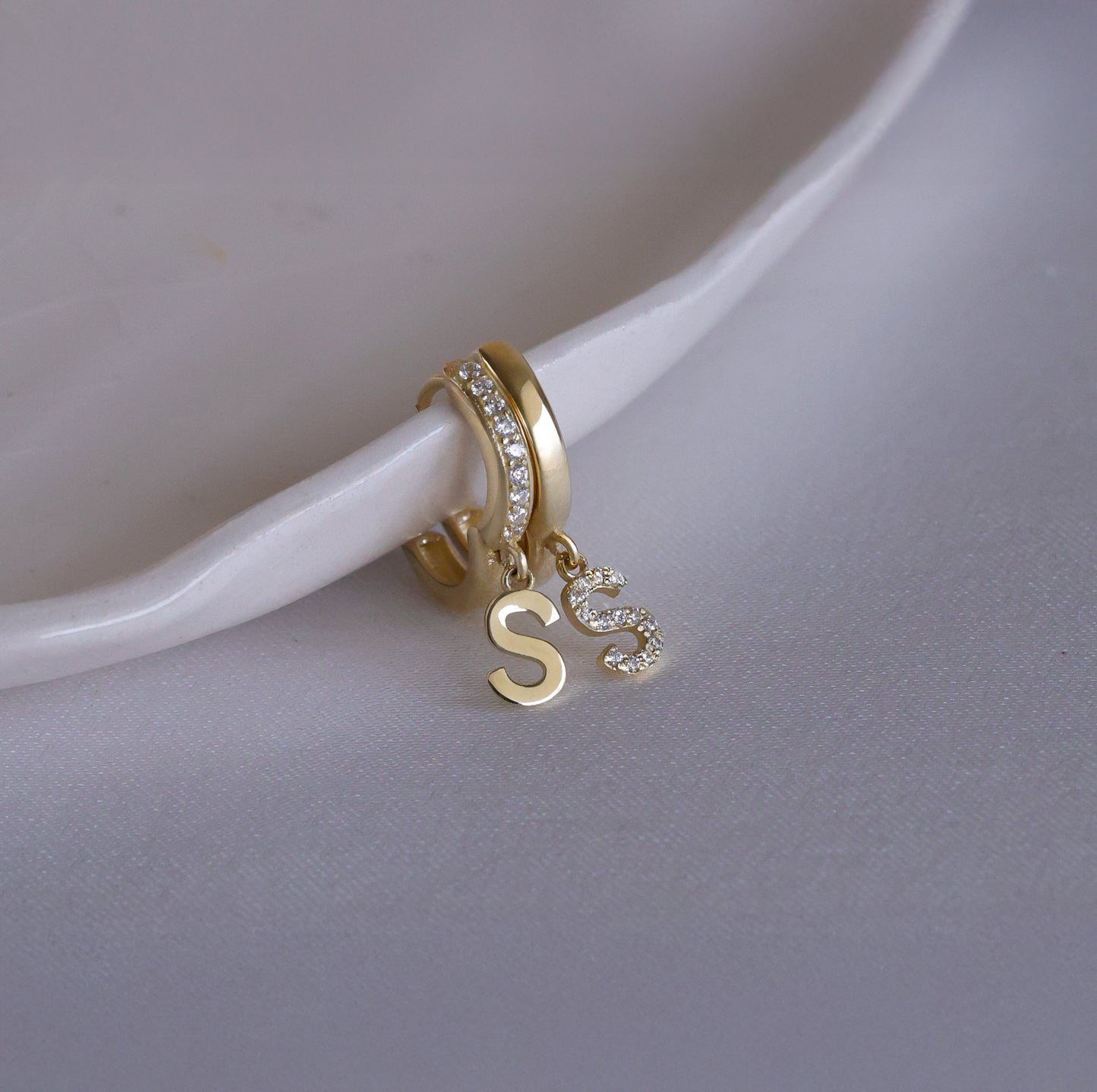 Mismatched set of gold huggie earrings featuring letter S charms.