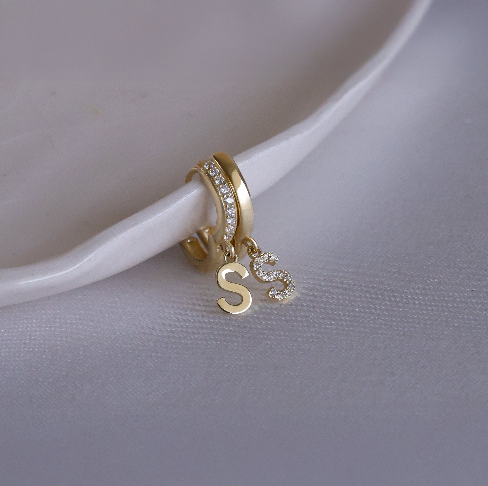 Mismatched set of gold huggie earrings featuring letter S charms.