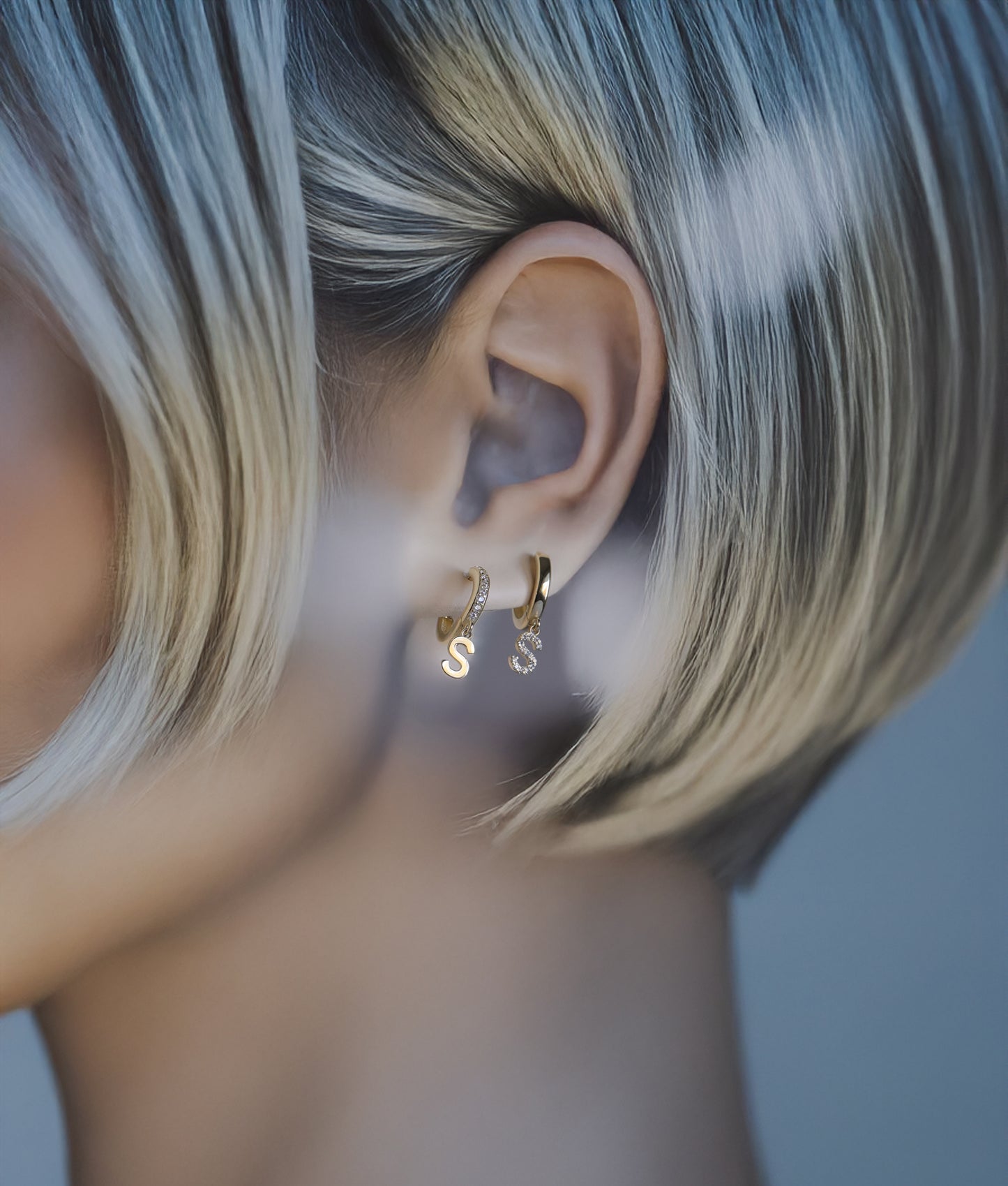 Model wearing solid gold initial dangle earrings with pavé diamonds.