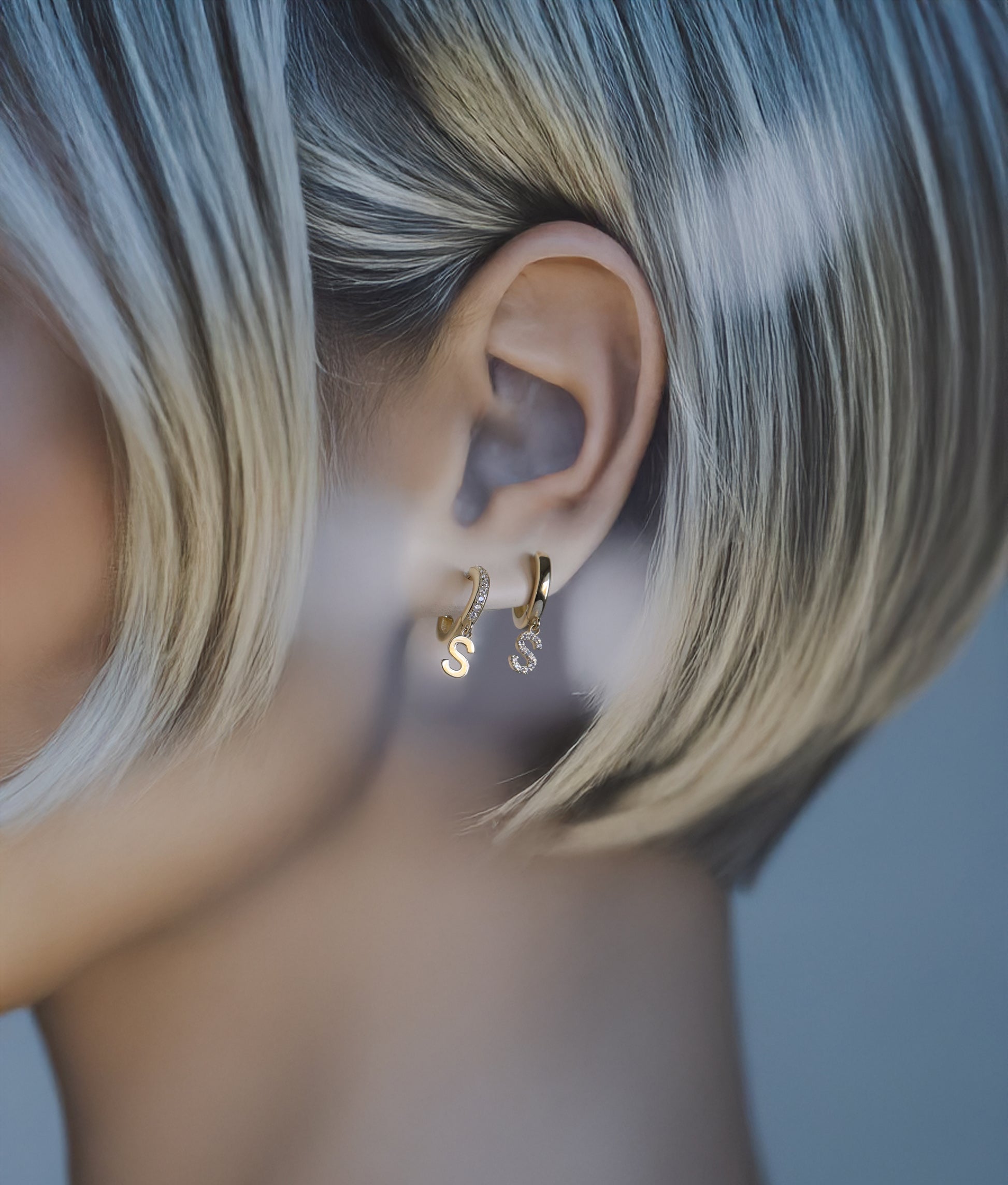 Model wearing solid gold initial dangle earrings with pavé diamonds.