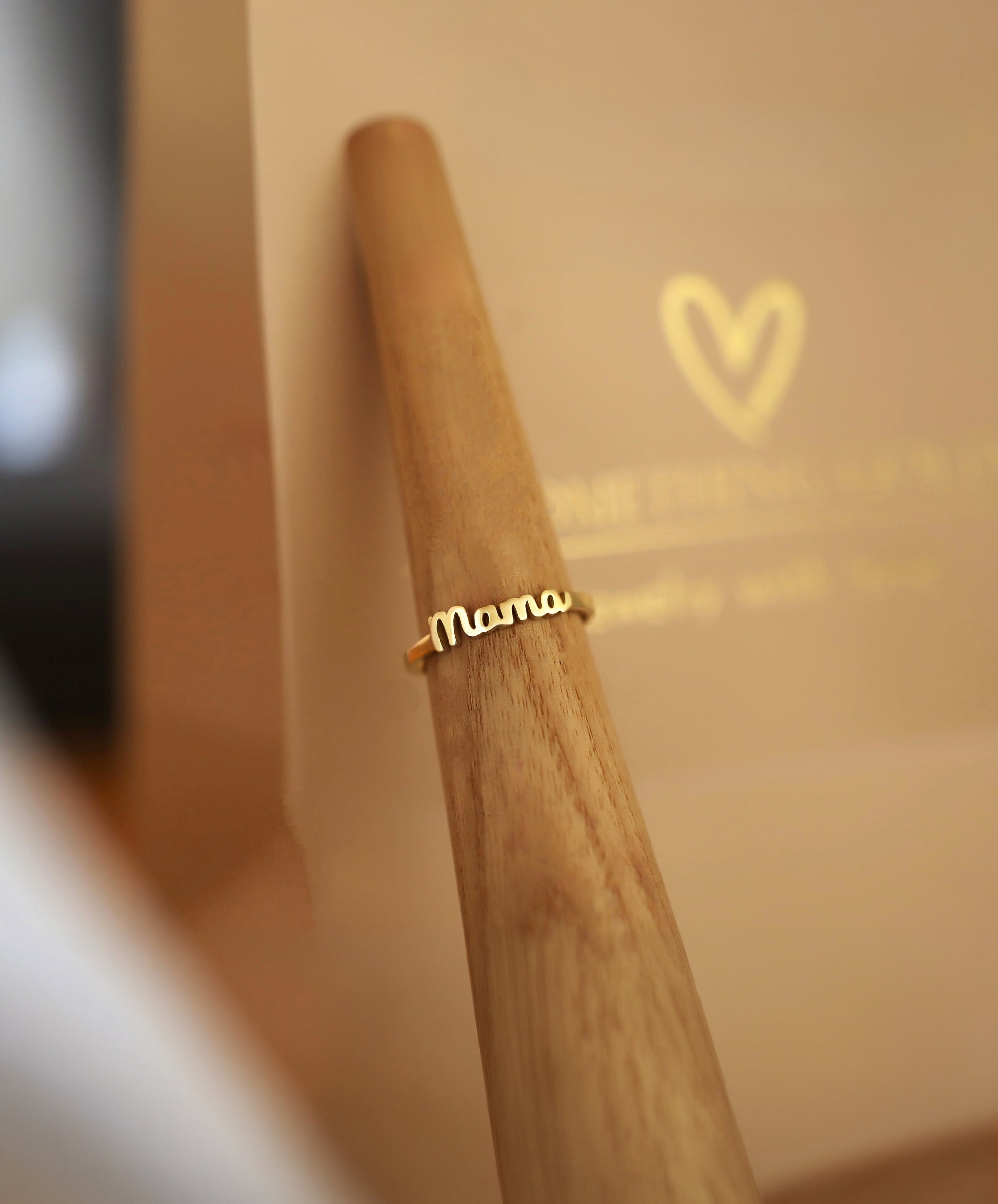 14k gold mama ring resting beautifully on a wooden ring cone display.