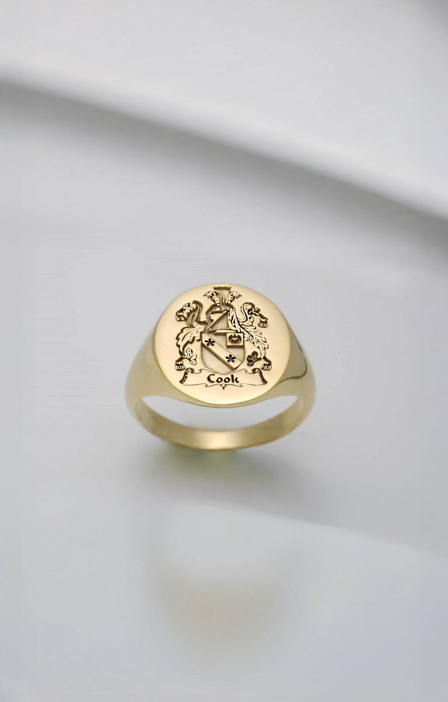 Gold signet ring with engraved family crest design on a light gray background