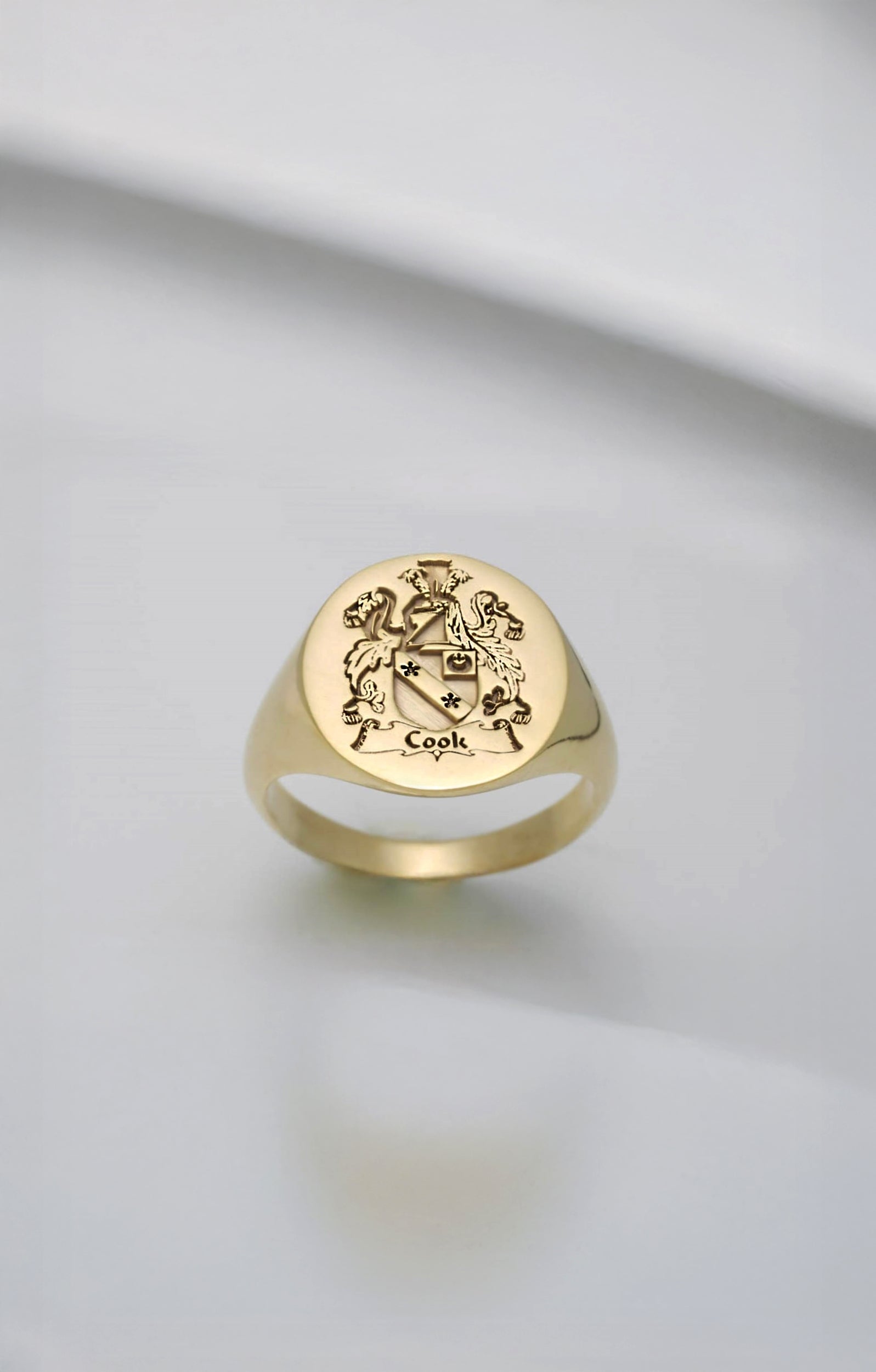 Gold signet ring with engraved family crest design on a light gray background