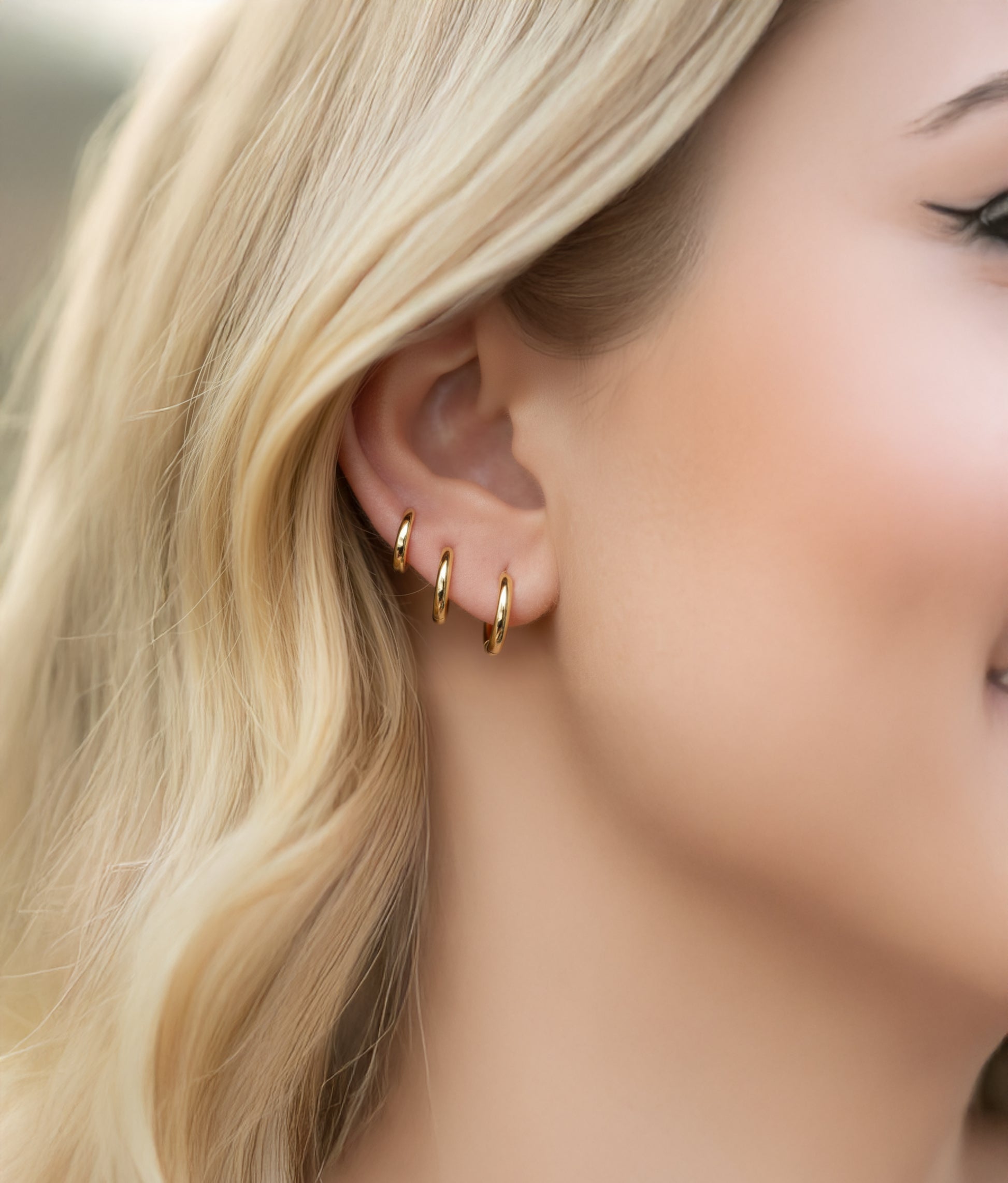 Model wearing a set of 3 graduated solid gold huggie hoops