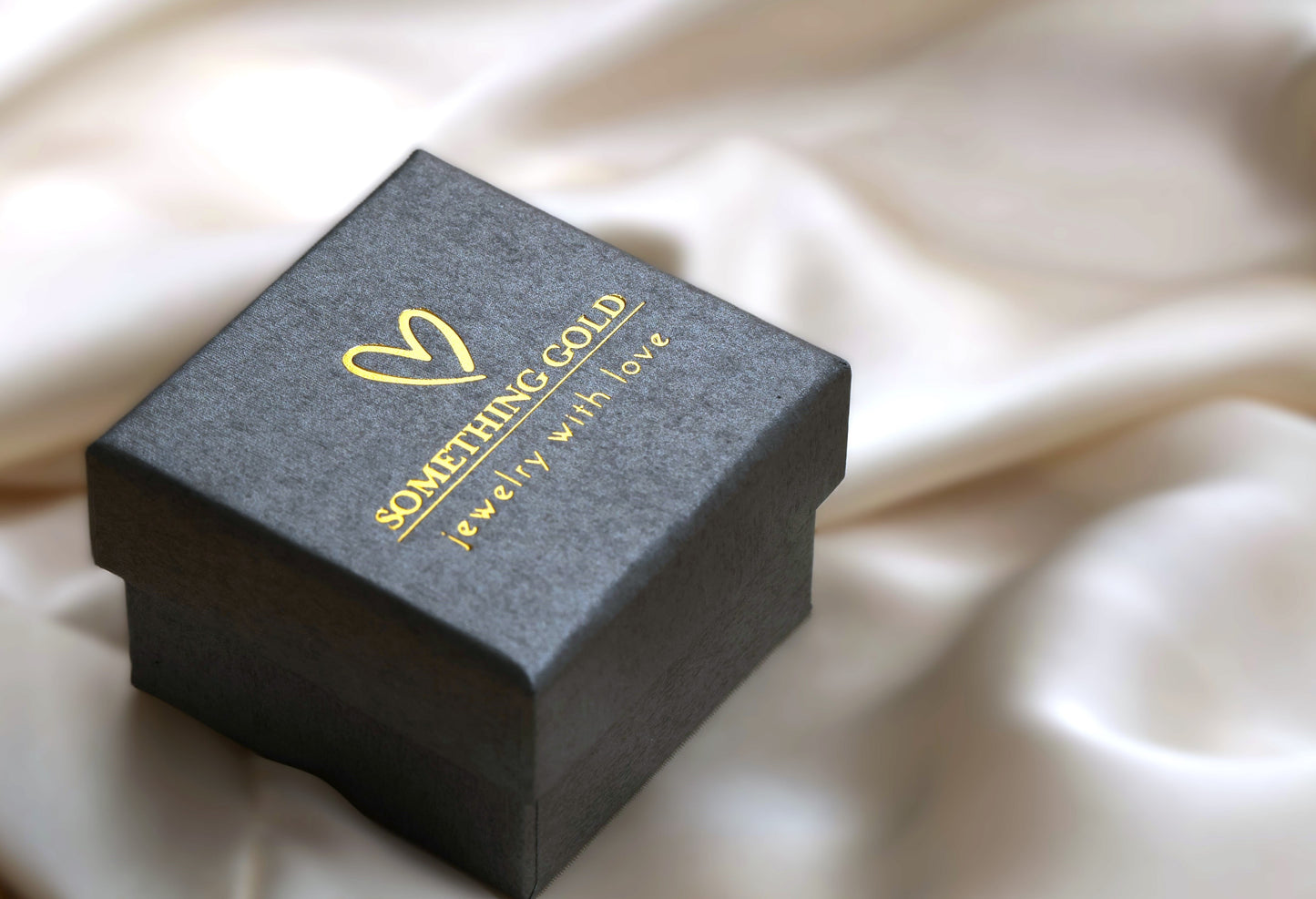 Jewelry box with 'Something Gold' branding on a beige fabric background