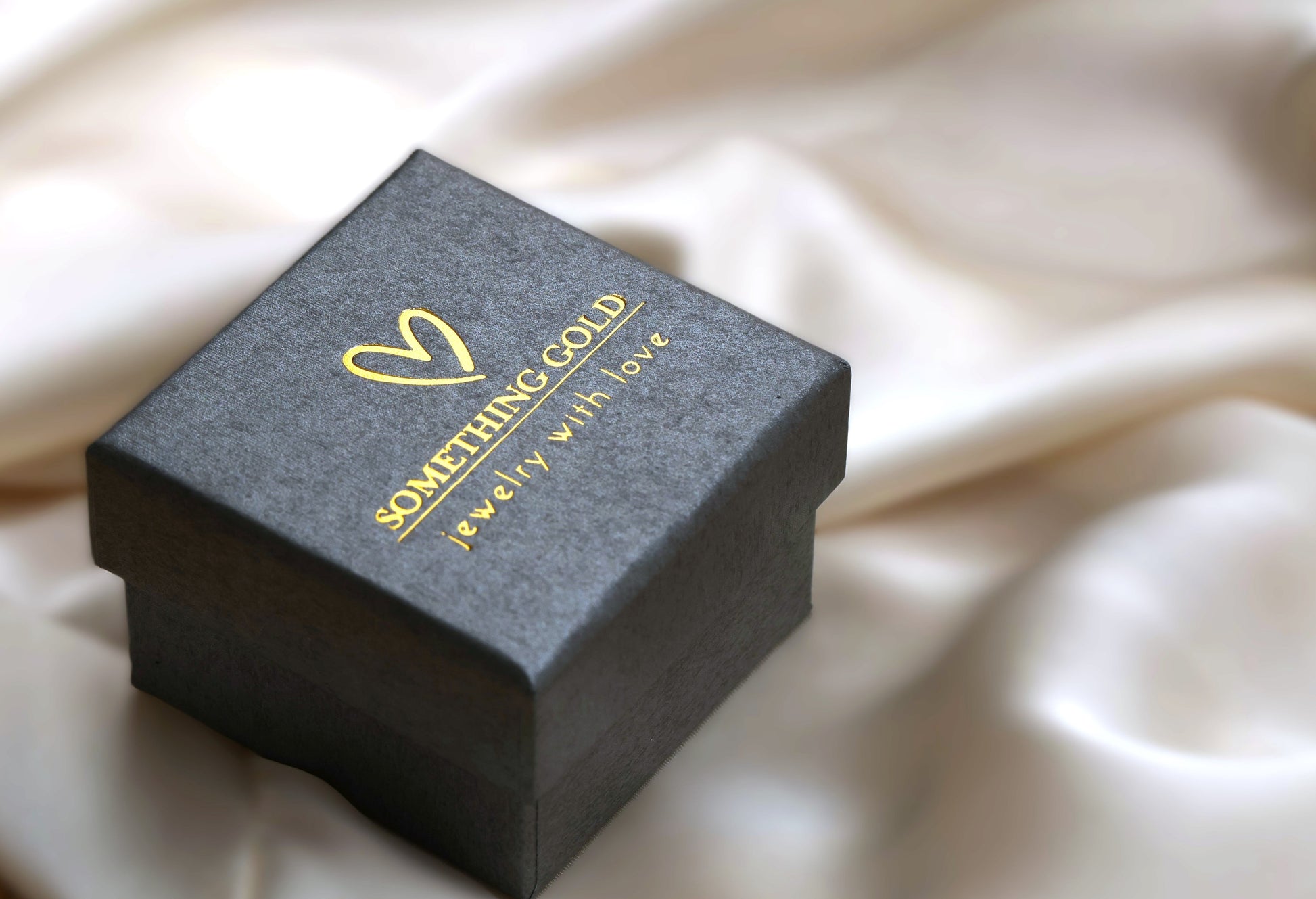 Jewelry box with 'Something Gold' branding on a beige fabric background