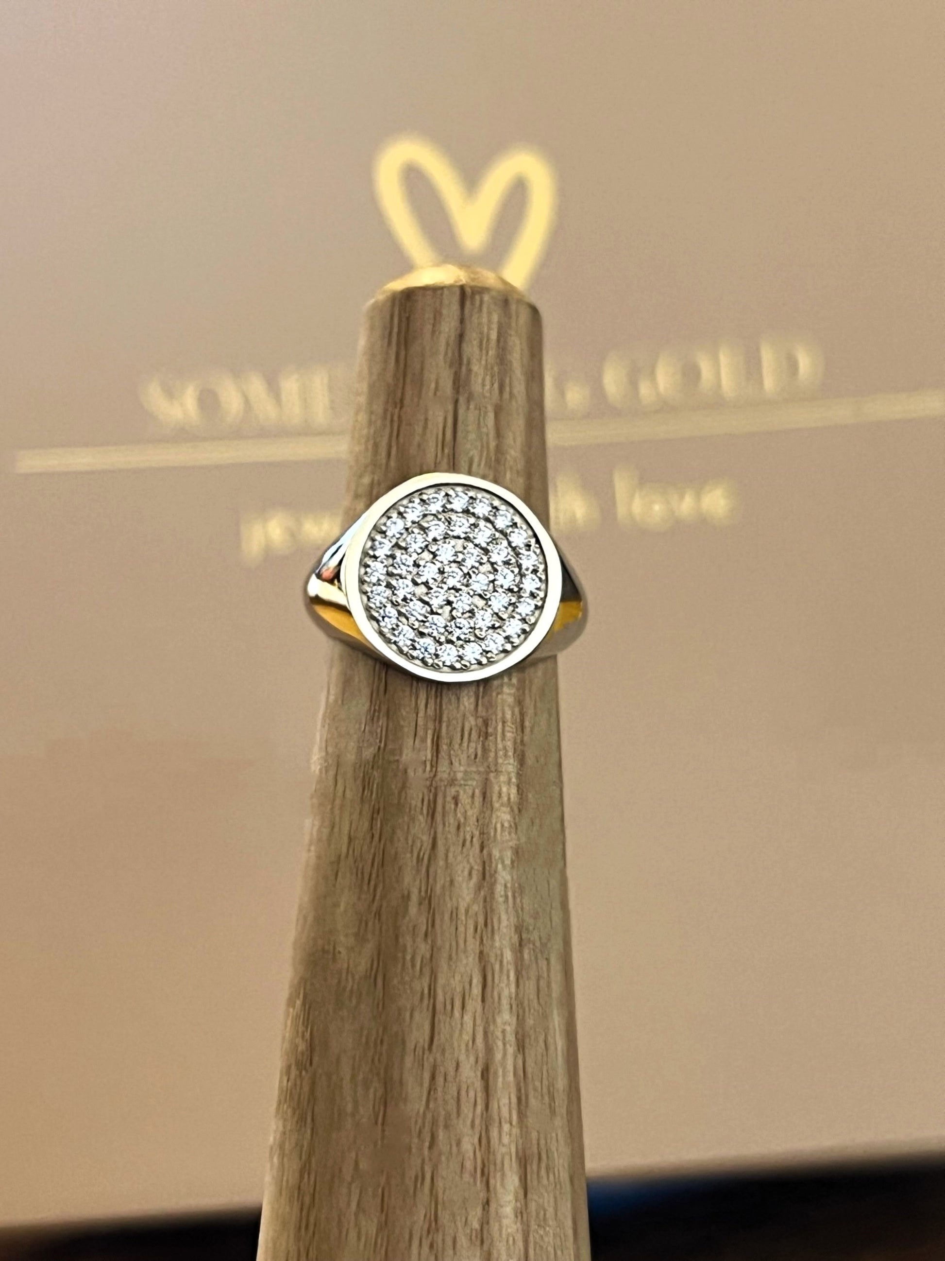 silver signet ring with diamonds on a wooden stand against a blurred background