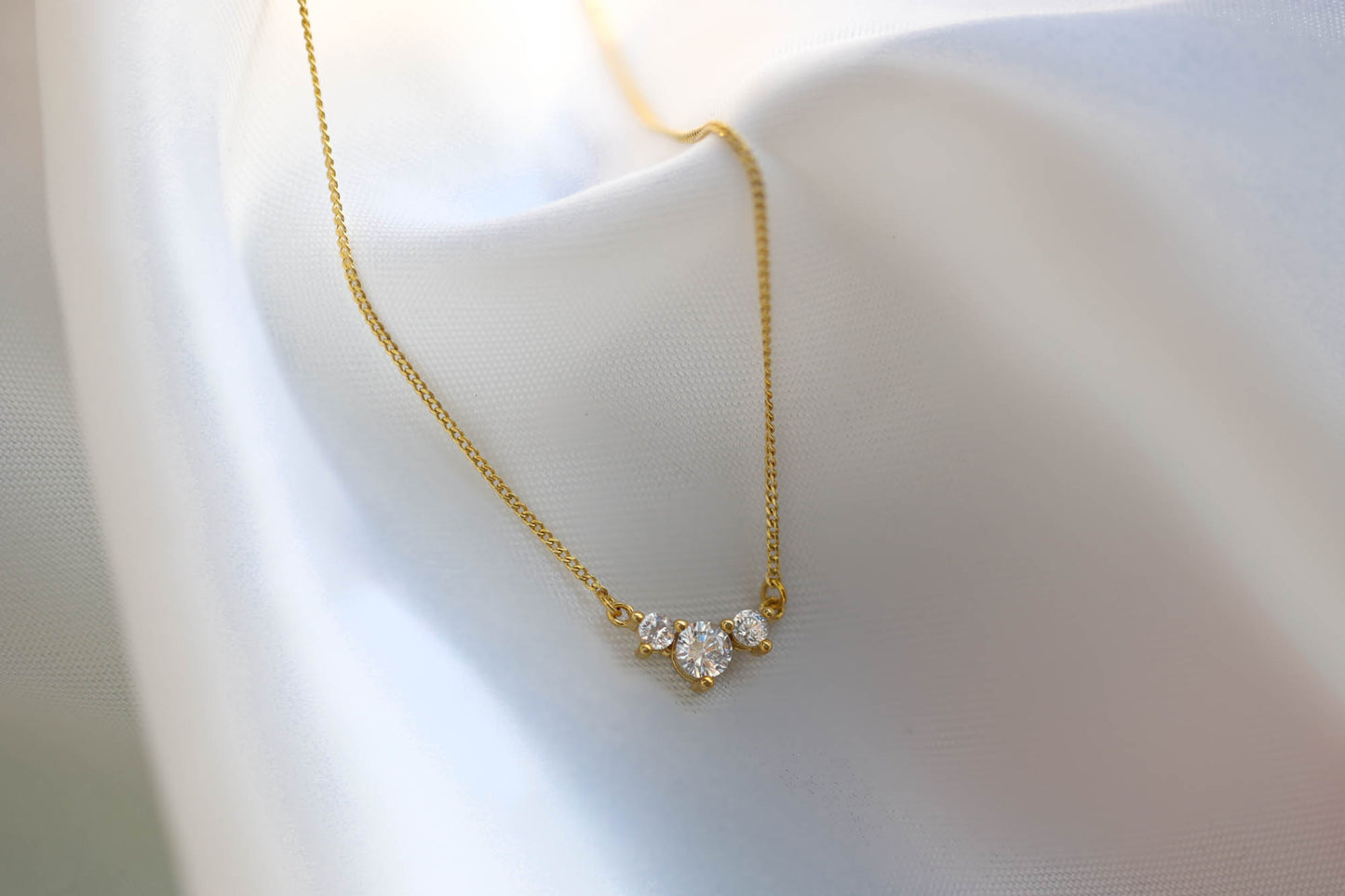 The minimalist 3 stone cz necklace shining brightly against smooth white silk fabric.